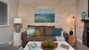 Una sala de estar acogedora con un sofá de cuero marrón, una pared de madera, un cuadro y una chimenea.