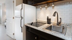 Una cocina moderna con refrigerador negro, salpicadero de azulejos blancos, encimera de granito, pileta de acero inoxidable y muebles negros.