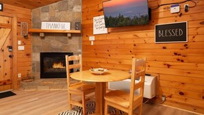A cozy cabin interior with a stone fireplace, wooden walls, a round wooden table with chairs, and motivational signs on the walls. - Gorgeous Mountain Views/Hot Tub (Sevierville)