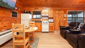 A cozy cabin interior with wooden walls, a kitchen area, a dining table with chairs, and a leather sofa. - Gorgeous Mountain Views/Hot Tub (Sevierville)