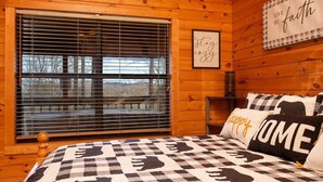 A cozy room with wooden walls, a large window with blinds, a bed with a checkered blanket, and a wall with motivational quotes. - Gorgeous Mountain Views/Hot Tub (Sevierville)
