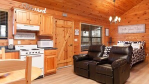 A cozy cabin interior with wooden walls and ceiling, a dining area with a table and chairs, a kitchen with a stove and microwave, and a seating area with leather couches. - Gorgeous Mountain Views/Hot Tub (Sevierville)