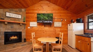 A cozy cabin interior with a stone fireplace, wooden walls, a round table with chairs, a kitchen area, and motivational wall signs. - Beautiful Mountain Cabin/Hot Tub (Sevierville)