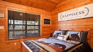 A cozy wooden cabin bedroom with a bed, a window with blinds, and a sign that says "HAPPINESS may nothing but come through our door." - Beautiful Mountain Cabin/Hot Tub (Sevierville)