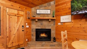 A cozy cabin interior with a stone fireplace, wooden walls, a 'Blessed' sign, and a 'be kind' sign. - Beautiful Mountain Cabin/Hot Tub (Sevierville)