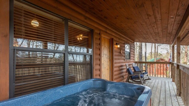 A wooden cabin with a hot tub on a deck, large windows, and a view of the forest. - Beautiful Mountain Cabin/Hot Tub (Sevierville)