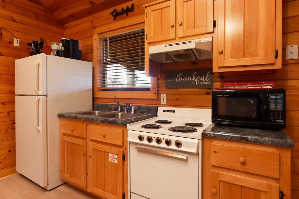 A kitchen with wooden cabinets, a white refrigerator, a stove, a microwave, and a window with blinds.