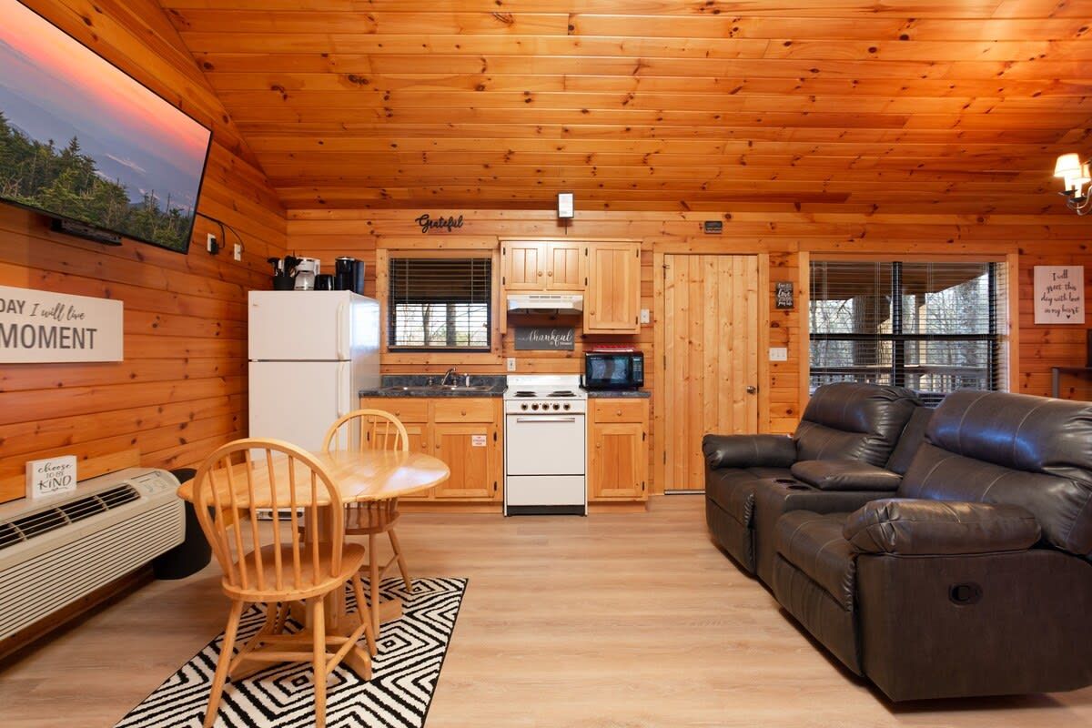 A cozy cabin interior with a kitchen, dining area, and a leather sofa.