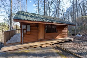 A small wooden cabin with a metal roof, a wooden deck, and a window.