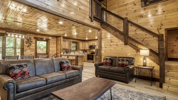A spacious log cabin interior with a living room, kitchen, and staircase.