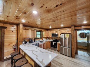 A kitchen with wooden cabinets, a central island, stainless steel appliances, and a window with blinds.