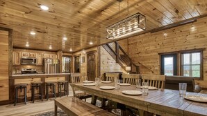 A wooden interior with a dining table set for six, kitchen area with appliances, and a staircase.