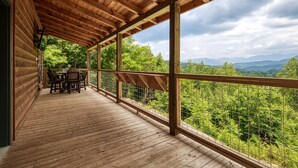 A wooden deck with a table and chairs, overlooking a forested landscape.