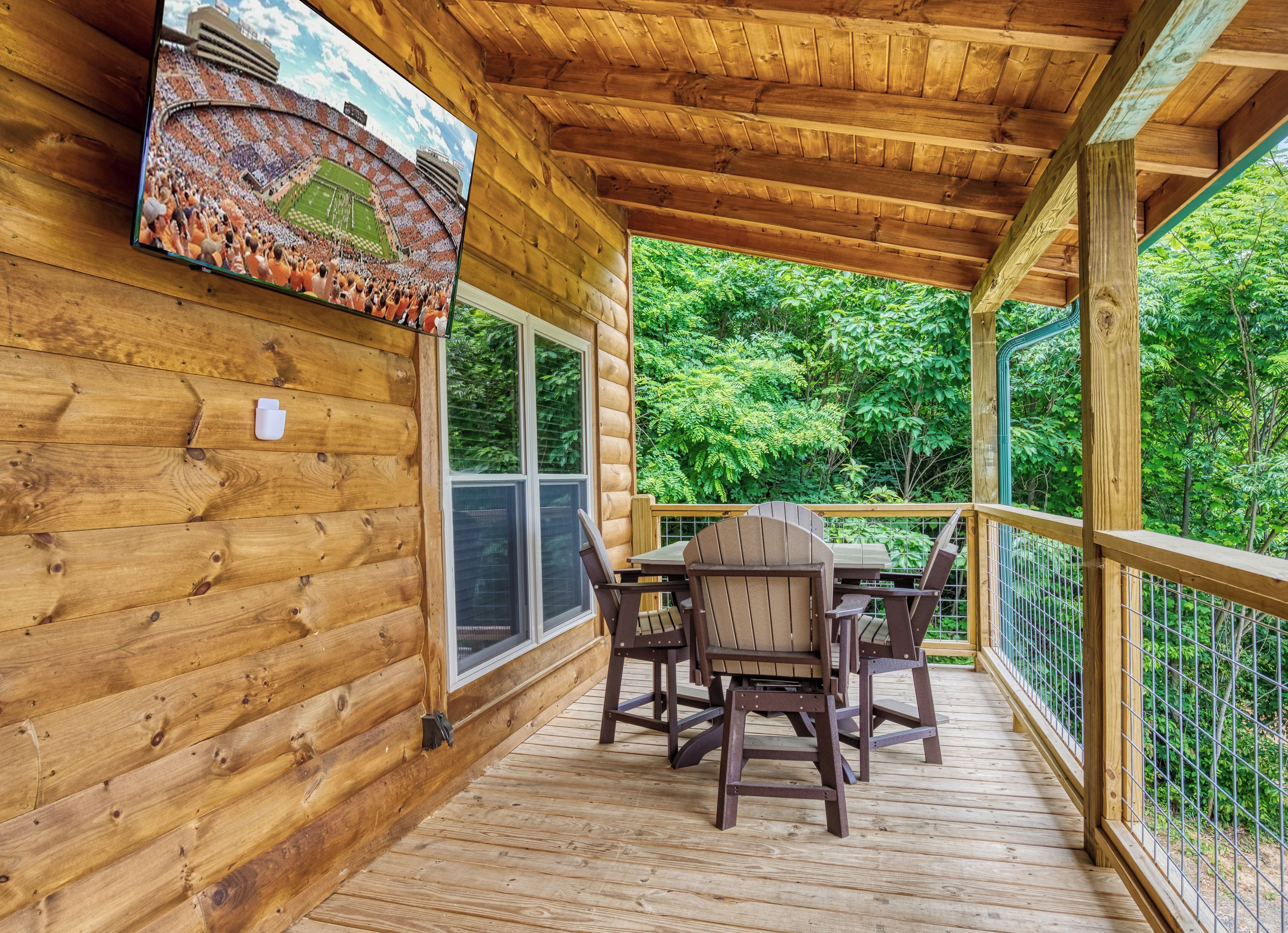 A wooden deck with a table and chairs, surrounded by a wooden railing, overlooking a lush green forest.