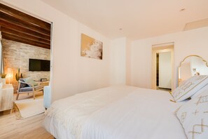 Un dormitorio con una cama grande, un televisor montado en una pared de piedra, techo de madera y una puerta que da a otra habitación.