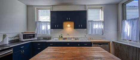 Une cuisine avec une table en bois, des meubles de rangement sombres, un four à micro-ondes et un évier.