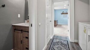 A hallway with a wooden cabinet, a white door, and a patterned rug leading to a room with a blue wall and a wooden cabinet.