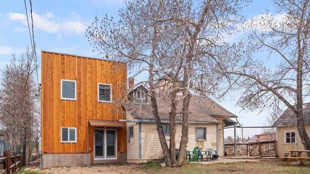 A modern wooden house with a covered porch, a small yard, and a tree.