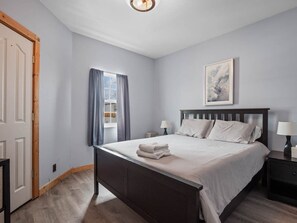 A bedroom with a bed, bedside tables, a window with curtains, and a framed picture on the wall. - Rustic 2BR Rocky Serene Mountain Escape. Fenced In (Leadville)