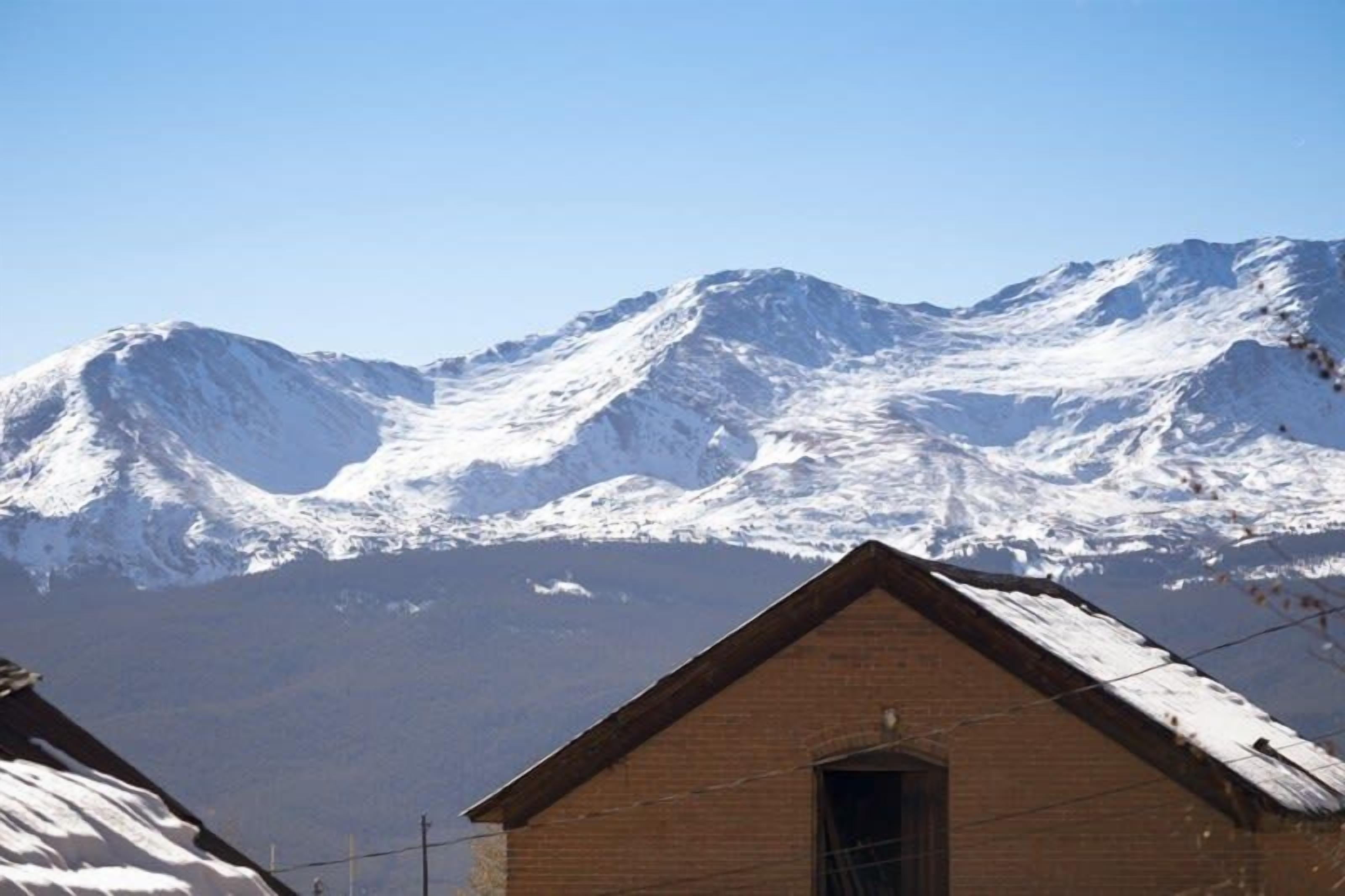 A mountain with snow-covered peaks in the background and a brick building in the foreground.