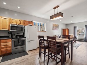 A modern kitchen with wooden cabinets, stainless steel appliances, and a dining area with dark wooden chairs. - Rustic 2BR Rocky Serene Mountain Escape. Fenced In (Leadville)