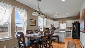 A modern kitchen with white cabinets, a central island, and a dining area with wooden chairs. - The Depot — Downtown Leadville Victorian, 3 Queens, Mt Elbert Views, Jetted Tub (Leadville)