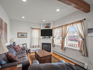 A living room with a sofa, a television, a fireplace, and large windows with curtains.