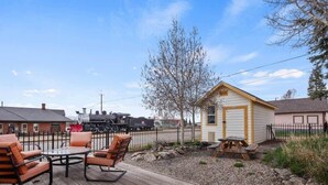 A wooden deck with outdoor furniture, a small shed, and a train in the background. - The Depot — Downtown Leadville Victorian, 3 Queens, Mt Elbert Views, Jetted Tub (Leadville)