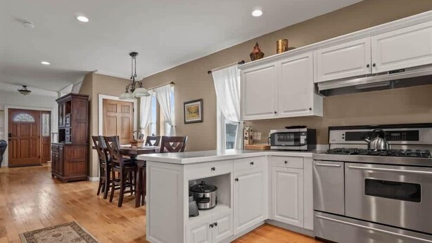 A modern kitchen with white cabinetry, stainless steel appliances, and a wooden dining area. - The Depot — Downtown Leadville Victorian, 3 Queens, Mt Elbert Views, Jetted Tub (Leadville)