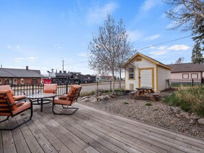 A wooden deck with outdoor furniture, a small shed, and a train in the background.