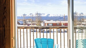 Un balcon avec vue sur des montagnes enneigées, un parking et un bâtiment avec un toit rouge.