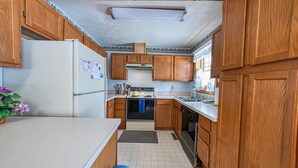 Una cocina compacta con armarios de madera, un refrigerador, estufa, fregadero y un pequeño bote de basura.