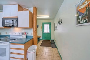 A compact kitchen with a microwave, stove, and wooden cabinets. A trash can and a small table are visible. - The Giddy Betsy — 3BR Cabin + Loft, Sleeps 8 near Twin Lakes & Mt. Elbert (Leadville)