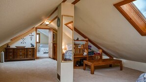 Un dormitorio acogedor en el ático, con techo inclinado, un banco de madera, un espejo y una estantería.