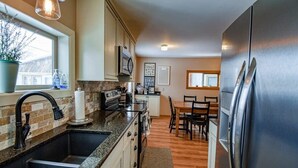 Una cocina moderna con encimeras de granito, electrodomésticos de acero inoxidable y un comedor con mobiliario de madera.