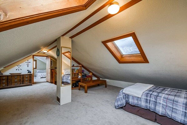 A bedroom with a sloped ceiling, a skylight, a bed, a desk, and a bookshelf.