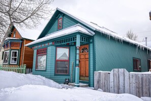 Une maison à deux étages, dont le toit est recouvert de neige, et qui est entourée d’une clôture en bois.