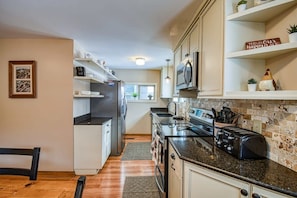 A modern kitchen with white cabinets, a black countertop, a refrigerator, a microwave, and a toaster. There is a window with a view of the outside.