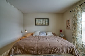 A bedroom with a large bed, a nightstand, a wall-mounted lamp, a fan, and a window with curtains. - The Ice Palace — 5BR Victorian Sleeps 12, Walk to Downtown Leadville (Leadville)