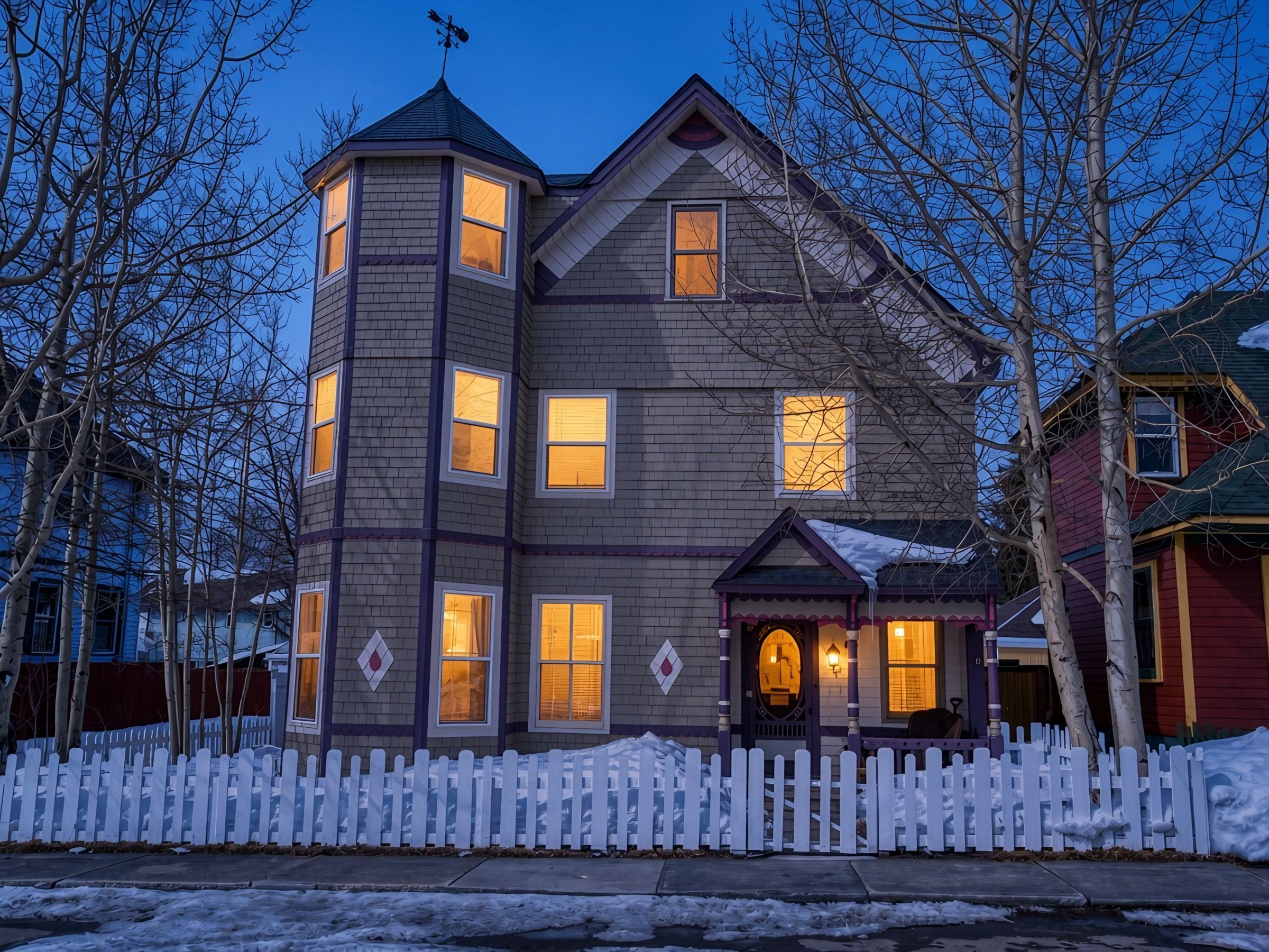 A multi-story house with a white picket fence, a turret, and a porch with a lamp.