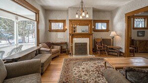 A cozy living room with a fireplace, wooden furniture, and large windows. - Josephine — Restored 4BR Victorian, Hot Tub, Walk to Main St Leadville, Sleeps 8 (Leadville)