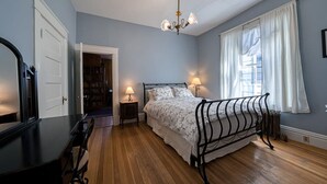 A bedroom with a bed, bedside lamps, a dresser, a mirror, and a door leading to a hallway. - Josephine — Restored 4BR Victorian, Hot Tub, Walk to Main St Leadville, Sleeps 8 (Leadville)