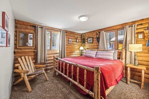 A log cabin room with a wooden bed, a chair, a lamp, and framed pictures on the wall. - 2BR Cabin–Deck Lake View & Access–BBQ, Pets OK! (Leadville)
