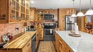 Cucina con pensili in legno, forno a microonde, piano cottura, frigorifero e un piano di lavoro in marmo.