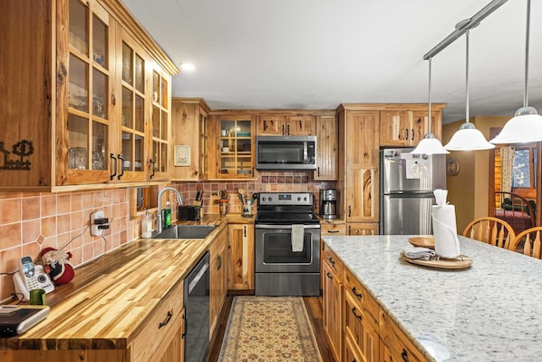 A kitchen with wooden cabinets, a microwave, stove, refrigerator, and a marble countertop. - 2BR Cabin–Deck Lake View & Access–BBQ, Pets OK! (Leadville)