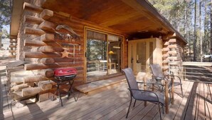 Una baita di legno con veranda, barbecue e posti a sedere all'aperto.