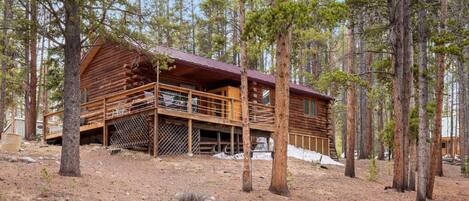 A log cabin with a wooden deck and a fire pit in front.