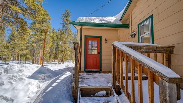 A wooden house with a red door, a wooden staircase leading to the entrance, and a snow-covered ground. - 3BR Cozy Cabin - Tranquil Forest - Pet Friendly (Leadville)