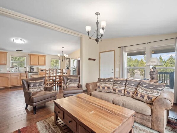 A spacious living room with a wooden coffee table, a sofa with patterned cushions, and a dining area with wooden chairs and a chandelier. - 3BR Mountain View - Covered Patio - Pet Friendly (Leadville)