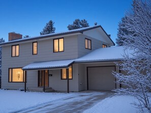 A two-story house with a garage, a covered porch, and a snow-covered driveway. - The Shamrock — 5BR Leadville Home, Game Room + 2-Car Garage, Sleeps 10 (Leadville)